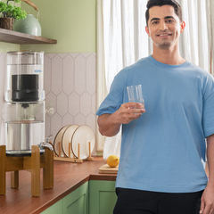 Man holding a glass of water in a kitchen with a water filter in the background
