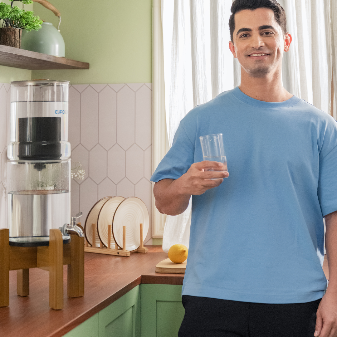 Man holding a glass of water in a kitchen with a water filter in the background
